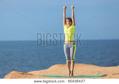 A young woman fitness trainer, shows a set of exercises with dumbbells.