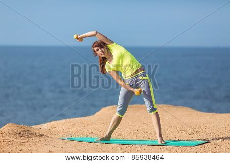 A young woman fitness trainer, shows a set of exercises with dumbbells.