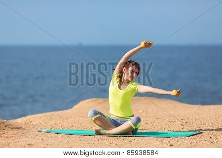 A young woman fitness trainer, shows a set of exercises with dumbbells.