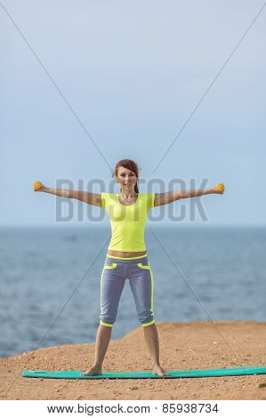 A young woman fitness trainer, shows a set of exercises with dumbbells.