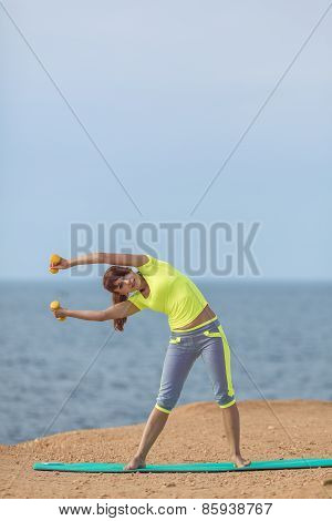 A young woman fitness trainer, shows a set of exercises with dumbbells.