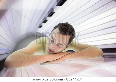 Handsome young man relaxing during a tanning session in a modern solarium, taking care of himself, enjoying the artificial sunlight.