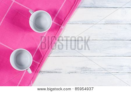 Two coffee cups on pink dishtowel and white wood background