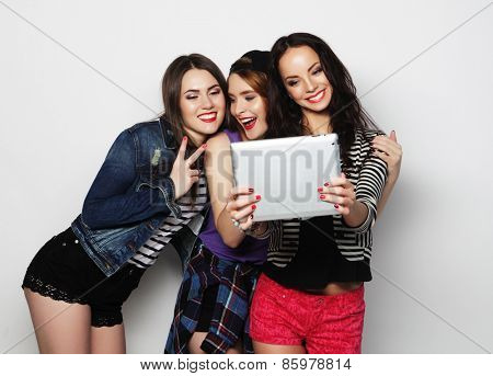 Three girls friends taking selfie with digital tablet, studio shot over gray vackground