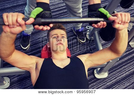 sport, fitness, equipment, lifestyle and people concept - men doing barbell bench press in gym with personal trainer or friend