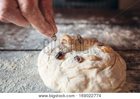 Decorating raw cake with dry fruits close-up. baker hand preparing sweet pie at kitchen, raw pastry with decoration on floured table. Cooking, bakery, culinary concept