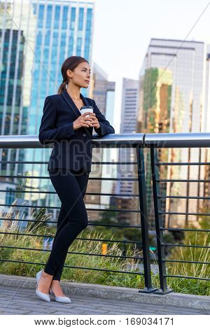 Businesswoman drinking coffee on break in business city center outside office buildings background. 
