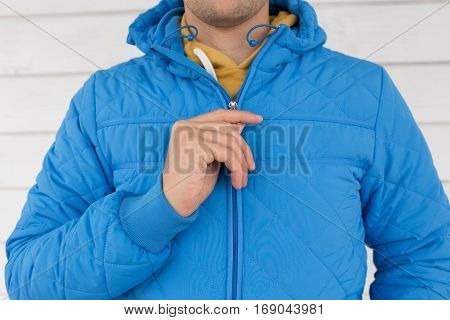 man buttons blue quilted jacket. cropped image of a man's hand fastens with a zipper on the jacket on a white background. close up
