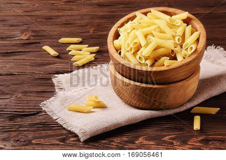 Raw pasta penne in a wooden bowl on the table