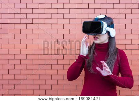 Handsome young woman using VR glasses with brickwall background and space for text