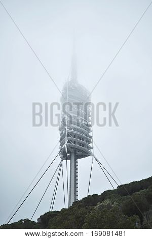 Vertical shot of big tv broadcasting tower station with many satellites on it , dissapears in fog above mountain forest