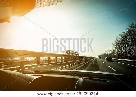 Car window view of trucks speeding in motorway with back sun light - Fast moving vehicles at sunset - Transportation concept - Focus on semitrucks and car - Warm filter with vignette editing