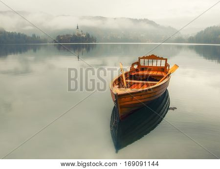 Lonely boat on the water surface of Bled lake at foggy autumn day, Slovenia