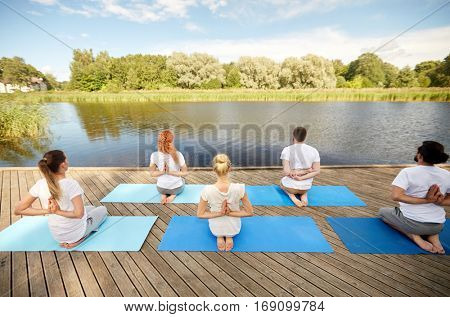 fitness, sport, yoga and healthy lifestyle concept - group of people exercising in reverse prayer pose on river or lake berth