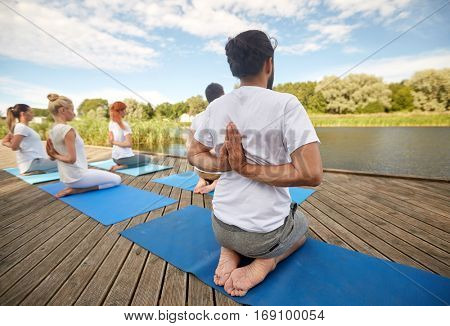 fitness, sport, yoga and healthy lifestyle concept - group of people exercising in reverse prayer pose on river or lake berth