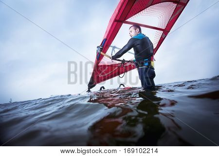 surfer standing in the water, waiting for the wind and waves before he steps up his surfboard