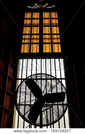 A fan positioned in an open window of a a huge historic church