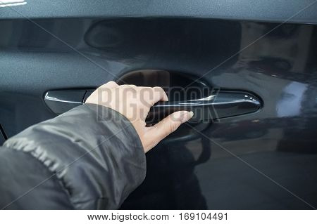 Female hand holding doorhandle a black car