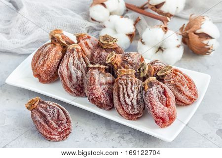 Several dried persimmon on white plate gray concrete background horizontal