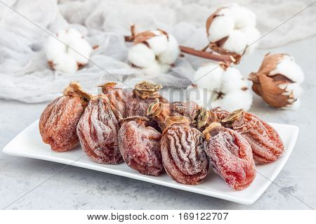 Several dried persimmon on white plate gray concrete background horizontal