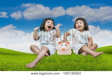Conceptual image happy child little girl sitting close a piggy bank in the grass and blue sky background.