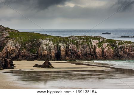 North Coast Scotland - June 6 2012: Durness Beach is a sandy patch looking north on a rough coast among rock cliffs and sprinkled pieces of rock. Under rainy sky with the light blue ocean gently flowing in.