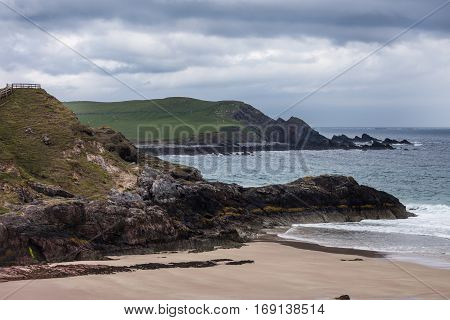 North Coast Scotland - June 6 2012: Cliffs descend on Durness Beach a sandy patch looking north on a rough coast among rock cliffs and sprinkled pieces of rock.