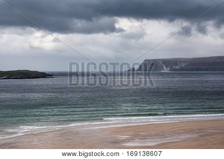 North Coast Scotland - June 6 2012: Huge cliffs tower over Durness Beach a sandy patch looking north on a rough coast among rock cliffs and sprinkled pieces of rock.