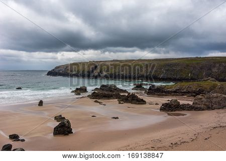 North Coast Scotland - June 6 2012: Cliffs descend on Durness Beach a sandy patch looking north on a rough coast among rock cliffs and sprinkled pieces of rock.