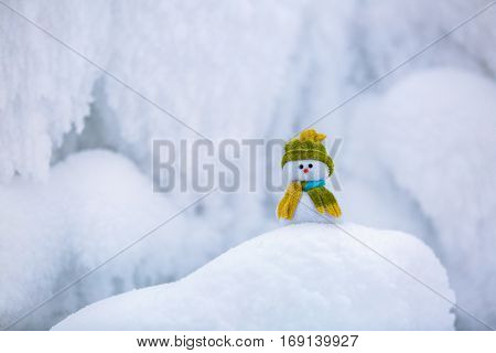 Fairytale character the snowman in hat and scarf is standing on fascinating fluffy snow near the hill and around there are frozen textured patterns.
