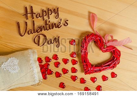 Heart sign Happy Valentine's Day on a wooden texture, and spilling out of the bag with small glass hearts