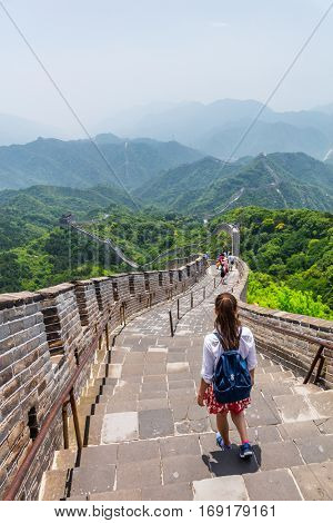 Woman backpacker student walking down the stairs overlooking the landscape of the Great Wall of China at famous Badaling tourist destination during travel vacation in Beijing. Asia summer holidays.