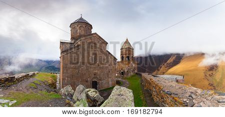 Gergeti Trinity Church Or Tsminda Sameba in the morning mist near village Stepantsminda, Georgia. Mount Kazbegi. Spring Or Summer Season.