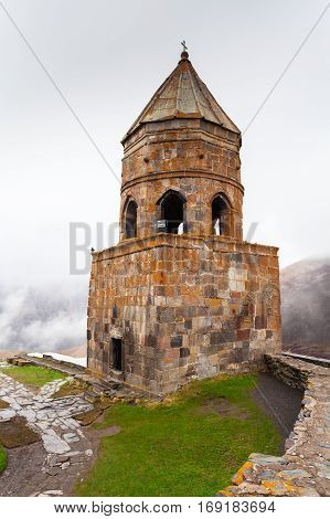 Gergeti Trinity Church Or Tsminda Sameba in the morning mist near village Stepantsminda, Georgia. Mount Kazbegi. Spring Or Summer Season.