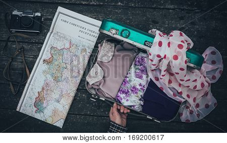 Vintage hipster suitcase packing before travel with old suitcase camera and accessories on a wooden table top view