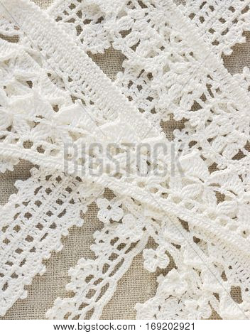 Handmade crocheted cotton organic lace ribbons on linen background. White original organic crochet frame Knitted pattern backdrop with handicraft work Mori Girl lace style. Needlework creative craft
