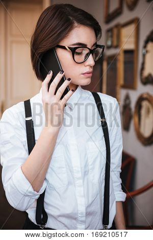 Vertical image of Authoress in glasses and white shirt talking on phone with closed eyes