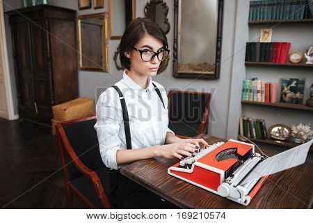 Side view of Authoress in glasses and white shirt using typewriting and looking at camera