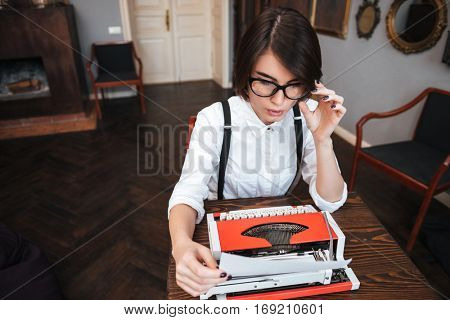 Top view of Authoress in glasses and white shirt sitting by the table and preparing typewriting