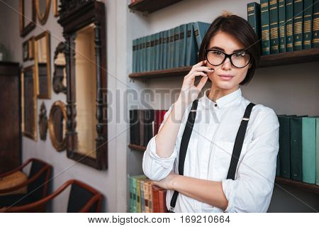 Authoress in glasses and white shirt standing near the bookshelf and looking at camera