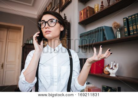 Pretty Authoress in glasses and white shirt talking on phone and looking up not understand gesture