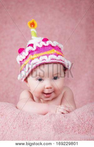 Newborn baby in warm knitted hat the form of cake with a candle.