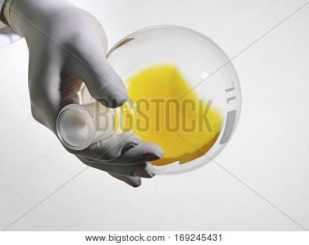 Closeup of lab worker's hand wearing rubber gloves holding flack of yellow solution on white background