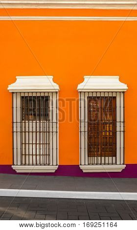 Two windows with bars on orange wall down the street