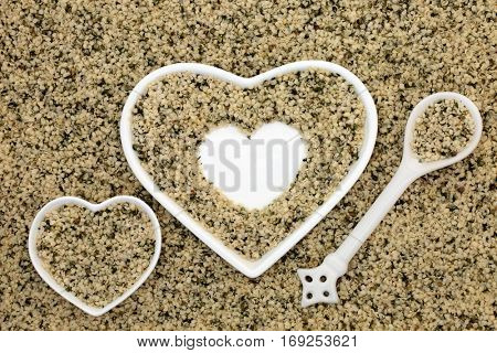 Hulled hemp seed health food in heart shaped dishes, spoon and loose forming a background.