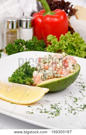 Avocado stuffed with mixture of marinated salmon with a cucumber on a white plate with fresh herbs