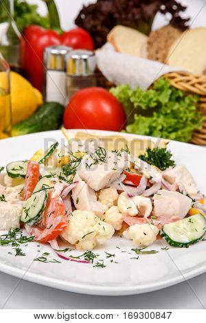 Fish salad with vegetables and spices on a white plate
