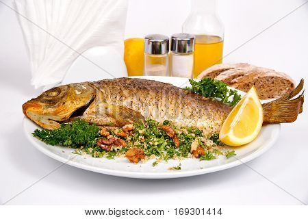 Carp stuffed with vegetables and raisins with greens and walnuts on a white plate