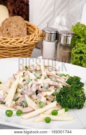 Russian salad with ham and smoked meats on a white plate with greens