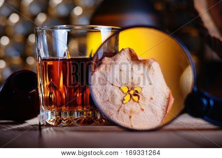 Glass of whiskey, magnifying glass, dried apple and smooking pipe